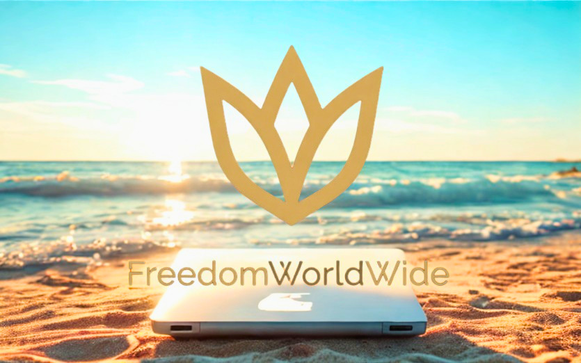 Gylden lotus-logo over solopgangsstrand, mens en åben hvid bærbar computer ligger på sandet. Arbejd online med hele verden som din arbejdsplads.